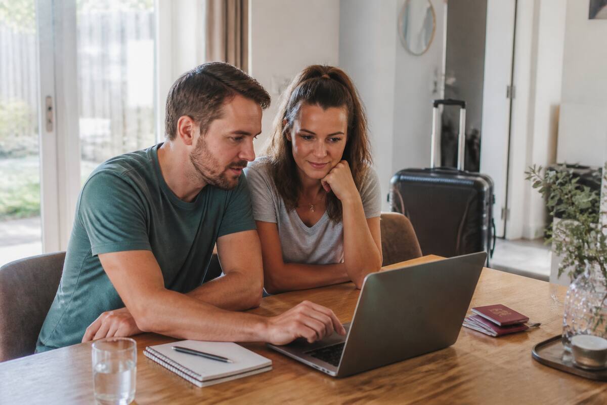 Gezin dat reisopties vergelijkt op laptop met notitieboekje en reisdocumenten